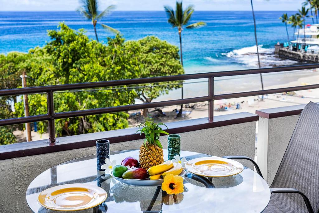 a table with a bowl of fruit on a balcony with the beach at White Sands Village#213 in Kailua-Kona