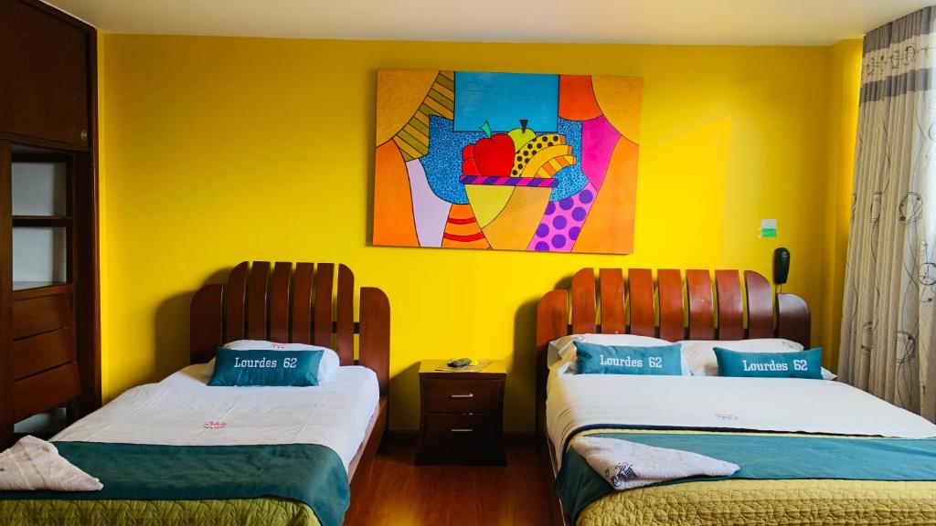 2 camas en una habitación con una pared amarilla en Hotel Lourdes la 62, en Bogotá