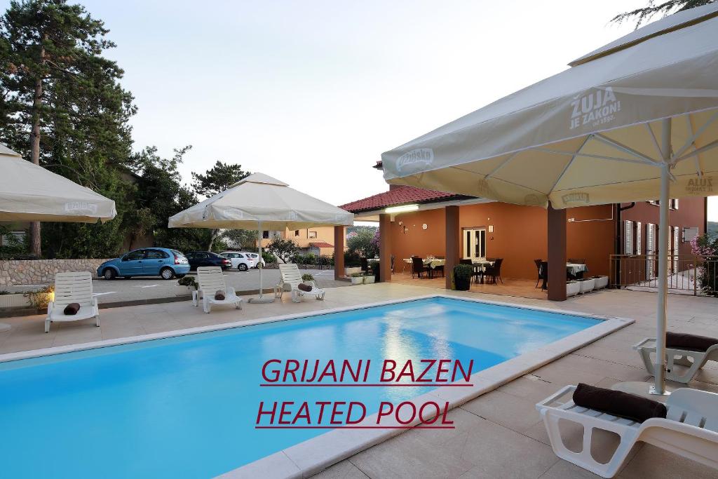 a swimming pool with chairs and umbrellas next to a house at Pension Riviera-Šilo in Šilo