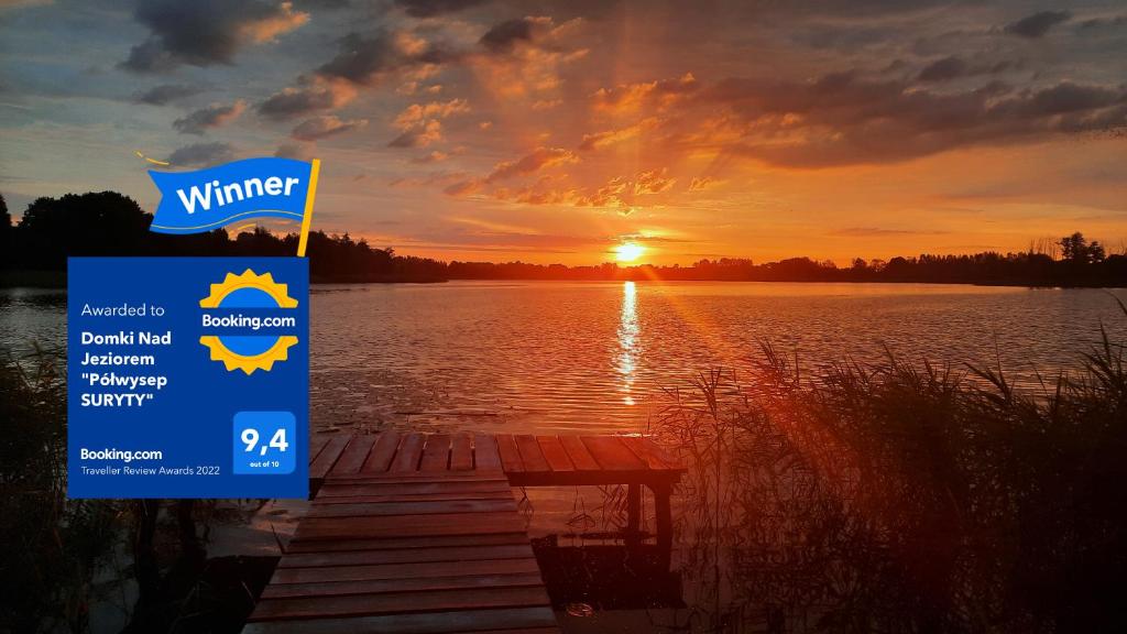 a sign in front of a lake with a sunset at Domki Nad Jeziorem "Półwysep SURYTY" in Suryty