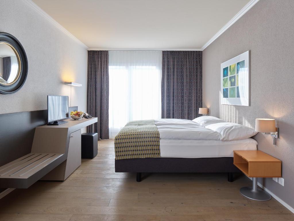 een slaapkamer met een bed, een bureau en een televisie bij Hotel Berchtold in Burgdorf