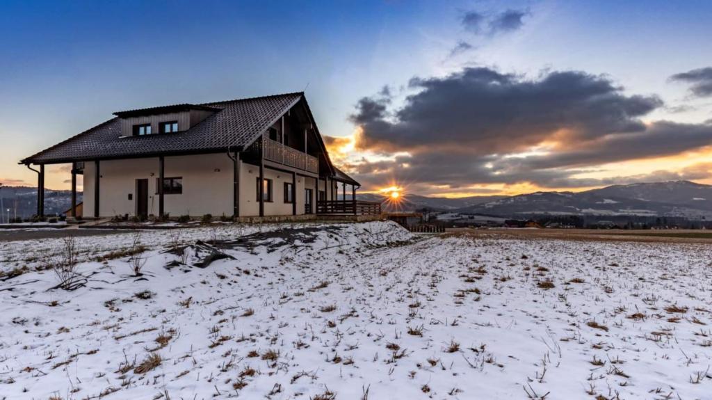 a house in a snowy field with the sunset in the background at Chata u Pinkasů in Jablunkov