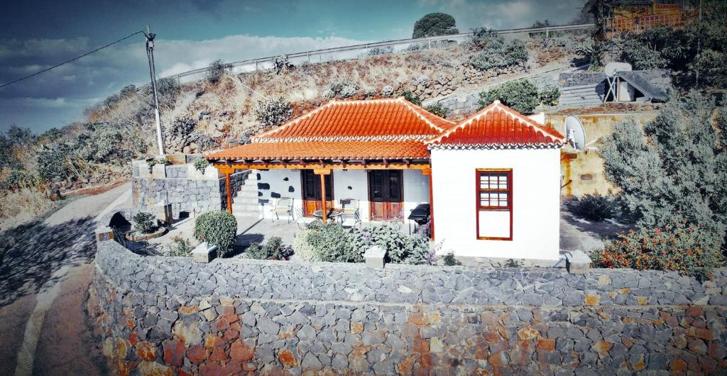 a small white house with an orange roof on a stone wall at Casa Micaela in Garafía