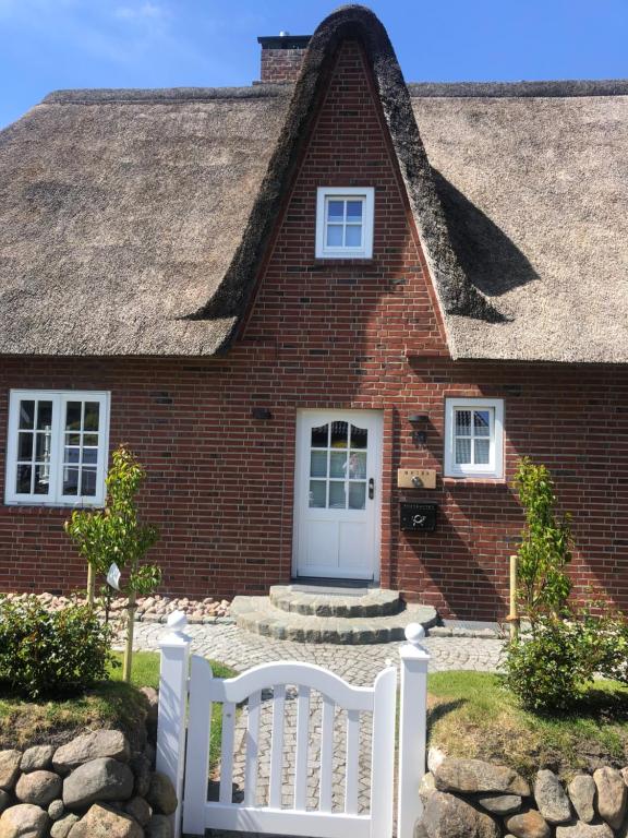 a house with a thatched roof and a white fence at Eidumhaus, freistehendes Reetdachhaus mit Garten in Strandnähe in Westerland (Sylt)