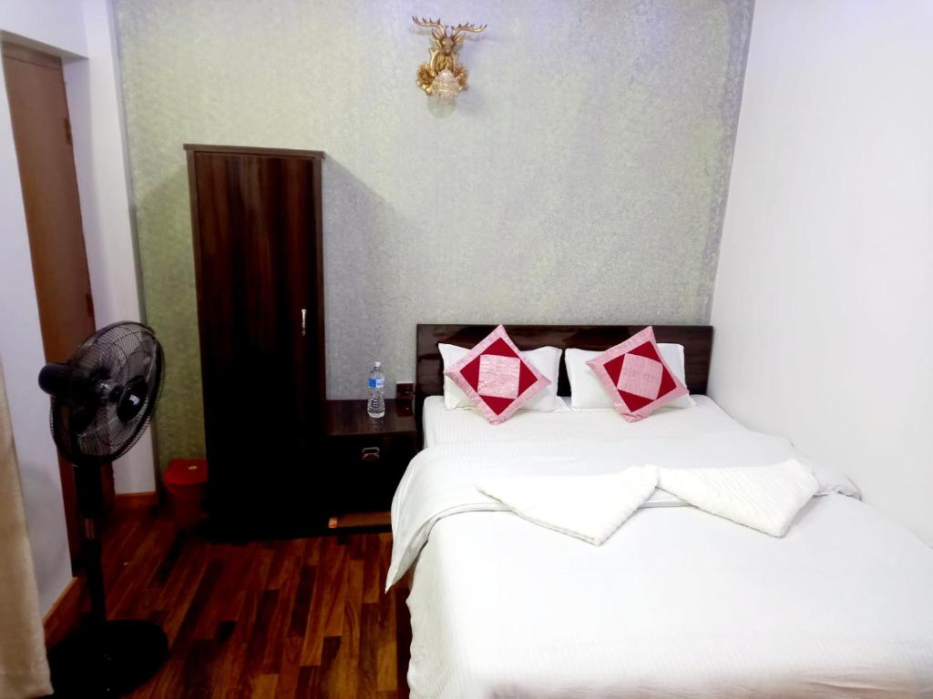 Serene B&B Kathmandu في كاتماندو: غرفة نوم بسرير ذو شراشف بيضاء ومخدات حمراء