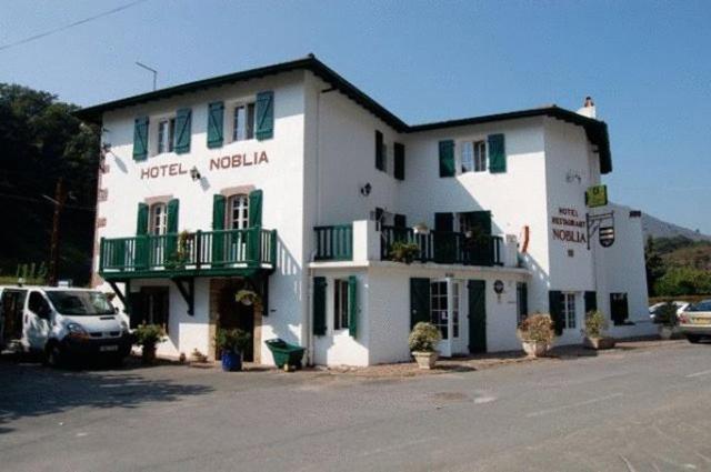 a large white building with green balconies on a street at Hotel Restaurant Noblia in Bidarray