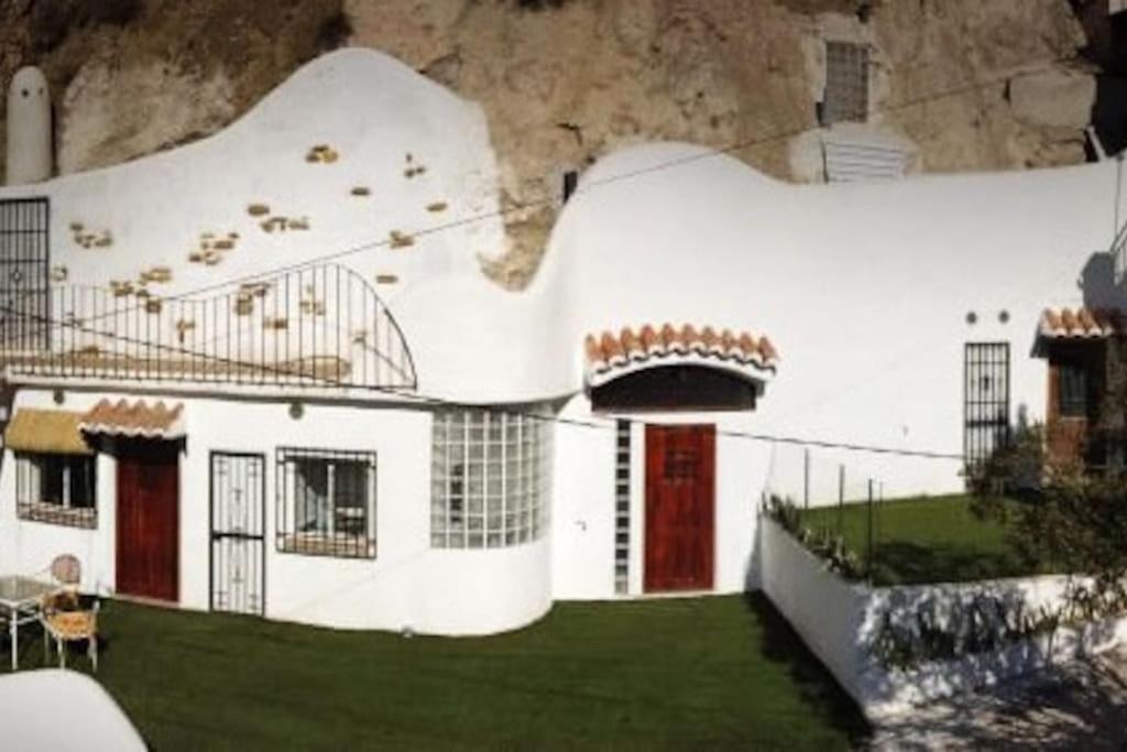 ein weißes Haus mit roten Türen vor einem Berg in der Unterkunft Las Cuevas de Monachil in Monachil