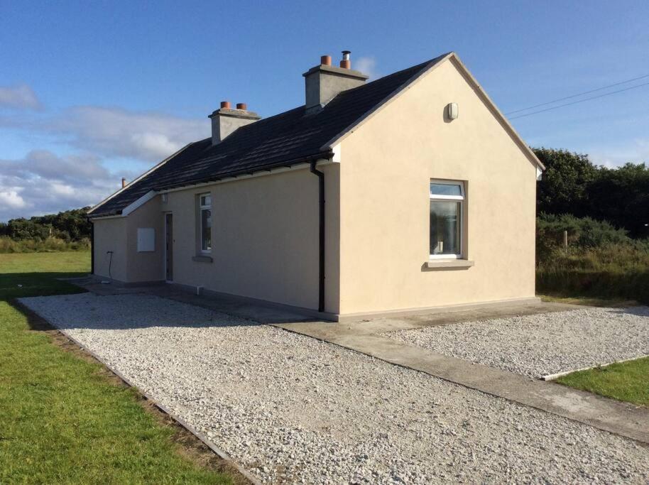 a small white house with a gravel driveway at Rossport bungalow with an Atlantic view in Ballina