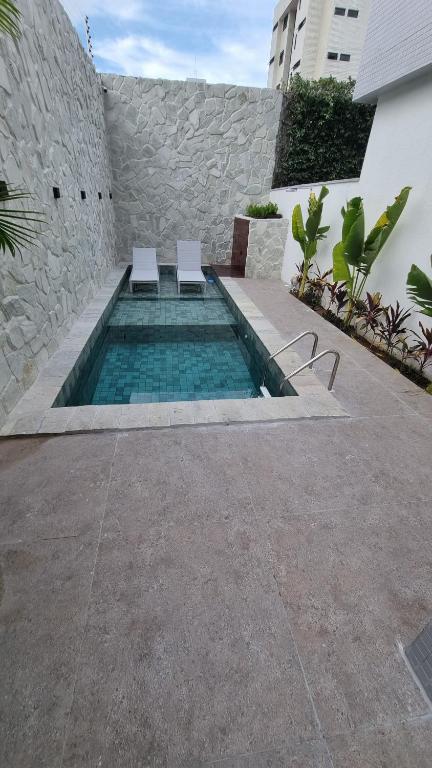 a swimming pool with two white chairs next to a building at Flat Bauten Cabo branco AP301 in João Pessoa
