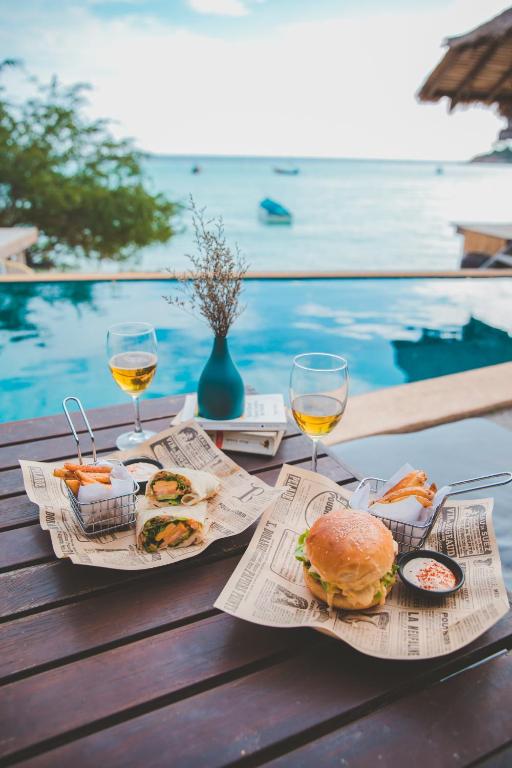 a table with two glasses of wine and a sandwich and food at New Heaven Dive School and Resort in Ko Tao