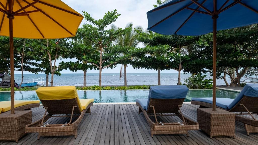 una terraza con sillas y sombrillas junto a una piscina en The Grand Villandra Resort en Lovina