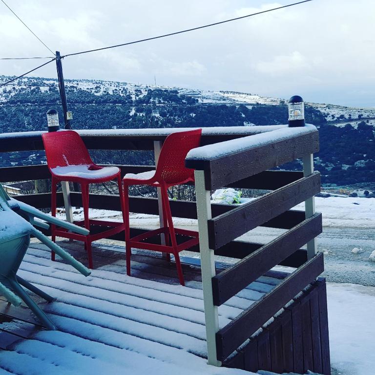 dwa czerwone krzesła stojące na tarasie w śniegu w obiekcie Sunset B&B w mieście Ein Kinya