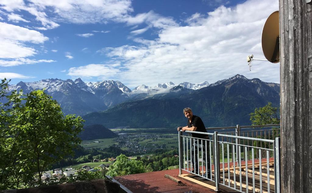 a man sitting on a balcony with a view of mountains at Sport- und Seminarhaus Walsertal in Thüringerberg