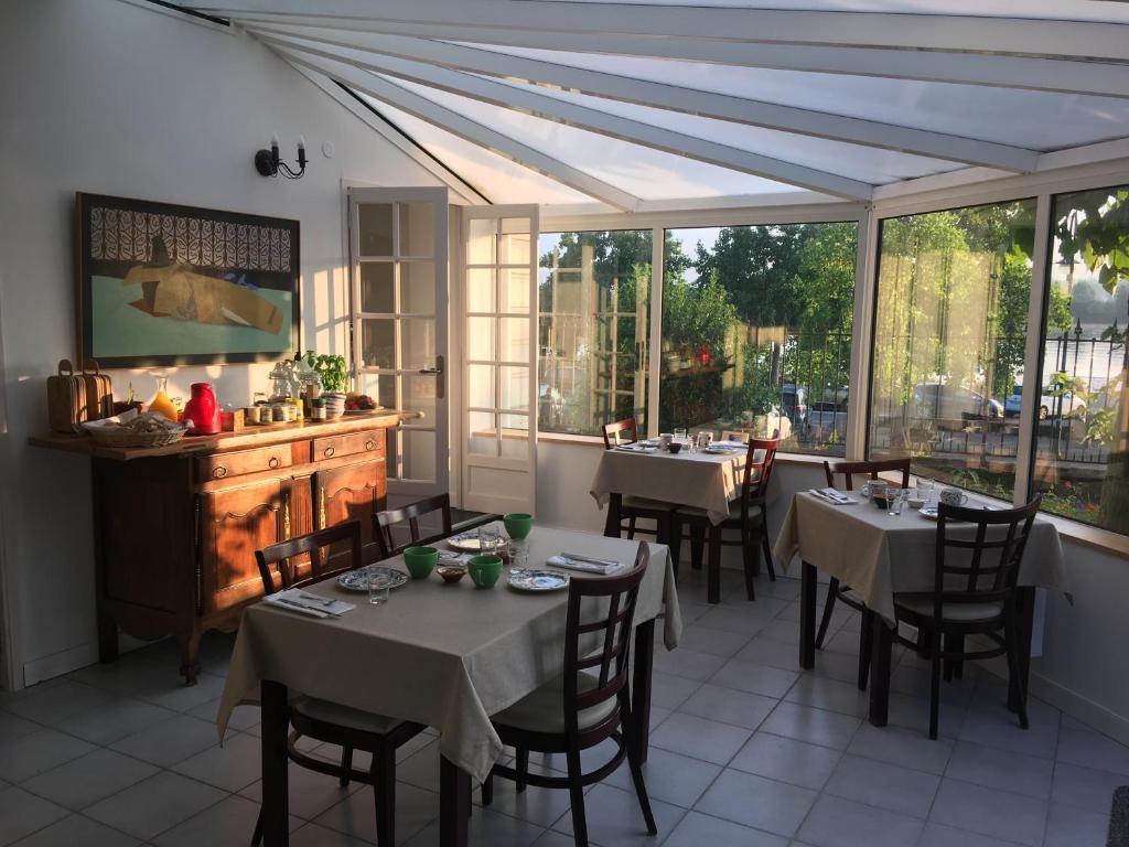 uma sala de jantar com mesas, cadeiras e janelas em La Houache Chambres d'Hôtes em Le Pellerin