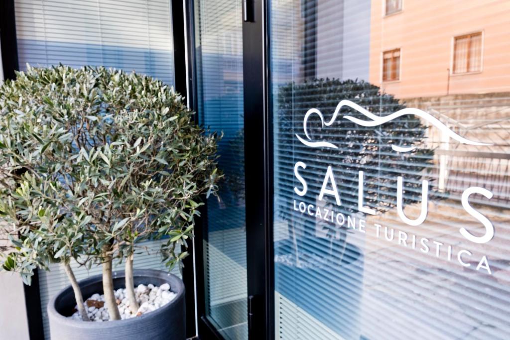 un cartello in una finestra di un negozio con un albero in vaso di SALUS Locazione Turistica a Verona