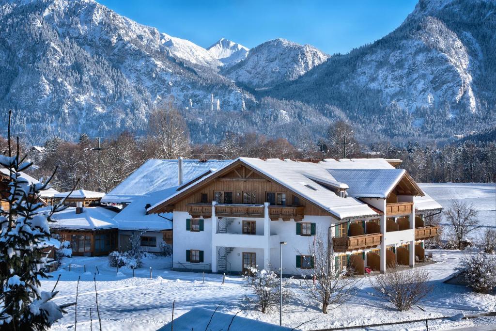 a house covered in snow with mountains in the background at Hotel Sommer-Haus am See in Füssen