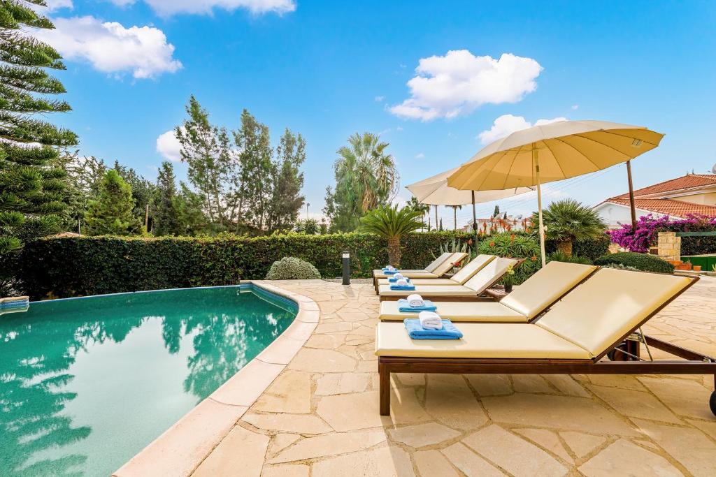 a pool with lounge chairs and an umbrella next to a swimming pool at Villa Camelot by Ezoria Villas in Coral Bay