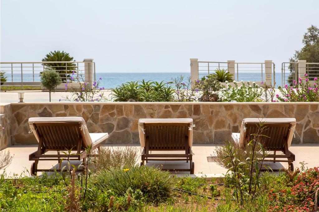 un gruppo di tre sedie seduti accanto a un muro di pietra di Thalassa Apartment Ierapetra a Ierápetra