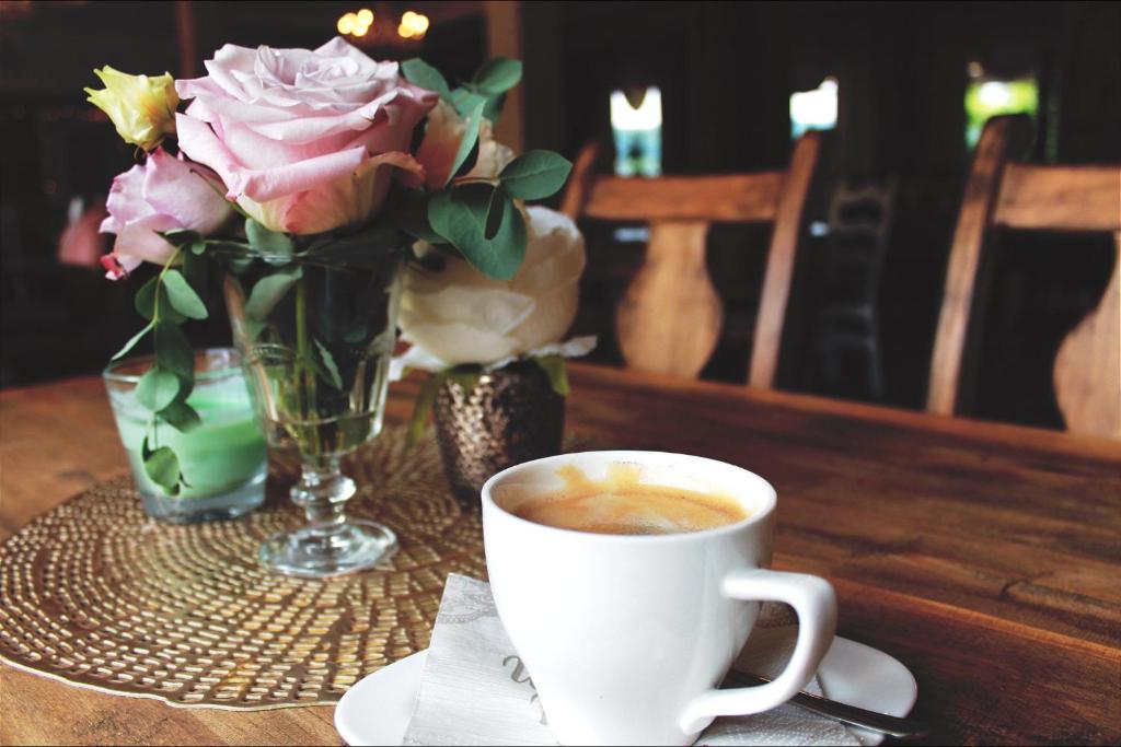 a cup of coffee and a vase of flowers on a table at Gasthof Via Vita in Treuchtlingen