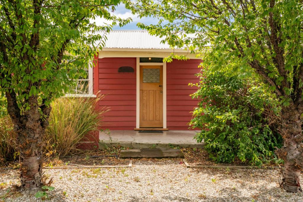 a red house with a yellow door between two trees at Cromwell Cutie - Cromwell Holiday Home in Cromwell