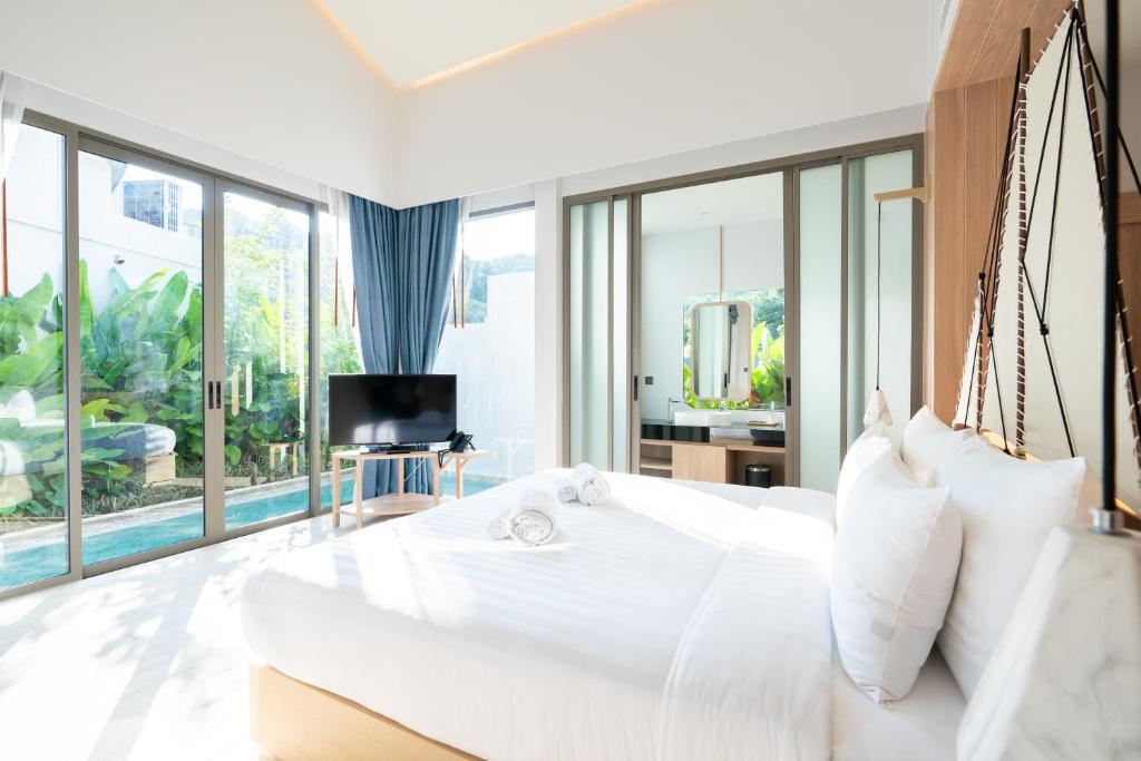 ein Schlafzimmer mit einem großen weißen Bett und großen Fenstern in der Unterkunft Panwaburi Beachfront Resort - SHA Extra Plus in Panwa Beach
