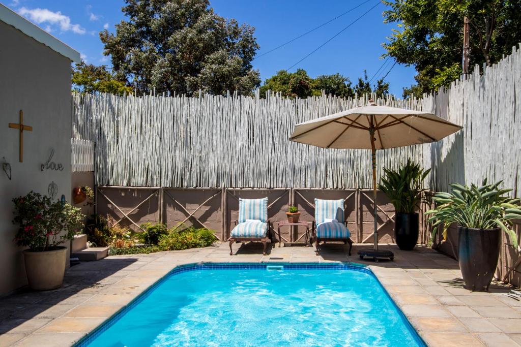 un patio trasero con piscina y sombrilla en The Potting Shed Guest House en Hermanus