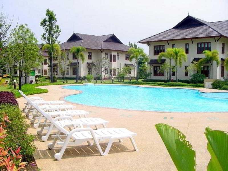 um grupo de espreguiçadeiras brancas ao lado de uma piscina em Teak Garden Resort, Chiang Rai em Chiang Rai