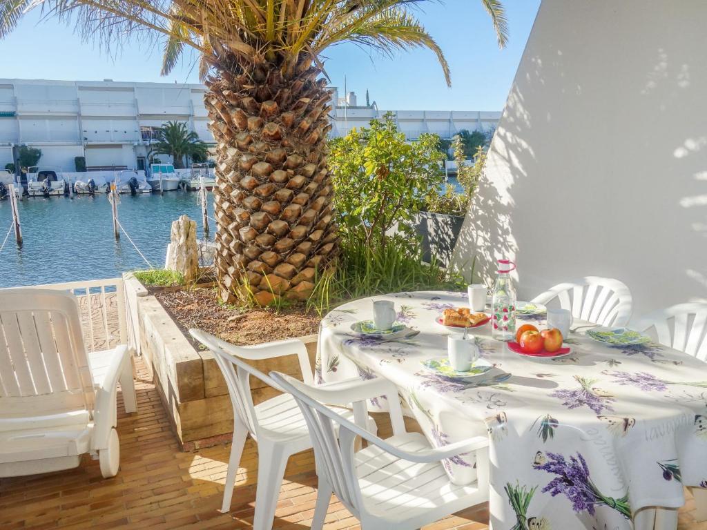 a table and chairs on a patio with a palm tree at Apartment Le Nirvana-1 by Interhome in Le Grau-du-Roi