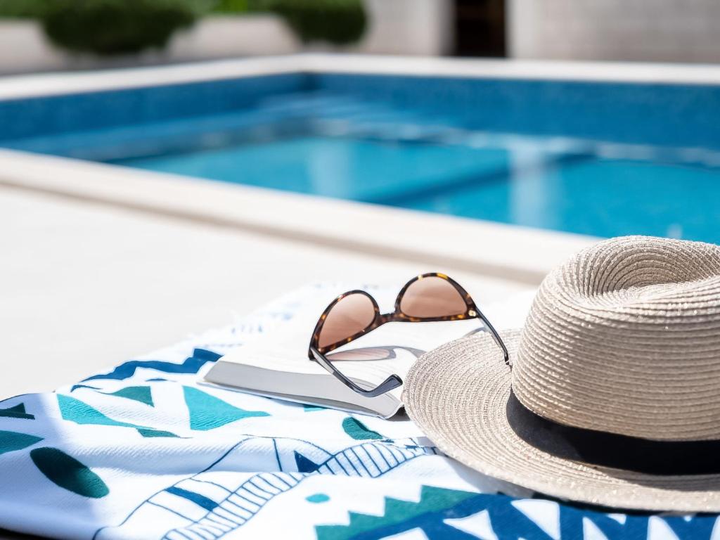 a straw hat and sunglasses sitting on a towel by a swimming pool at Apartment Villa 2 Pools-5 by Interhome in Sutivan