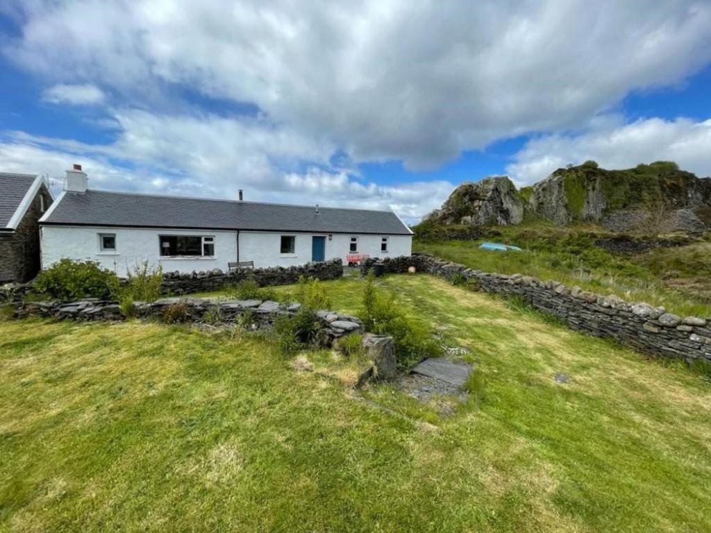 a white house in a field with a stone wall at Holiday Home Easdale Cottage by Interhome in Oban