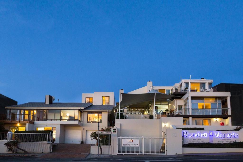 a large white house with a sign in front of it at Blaauw Village Guest House in Bloubergstrand