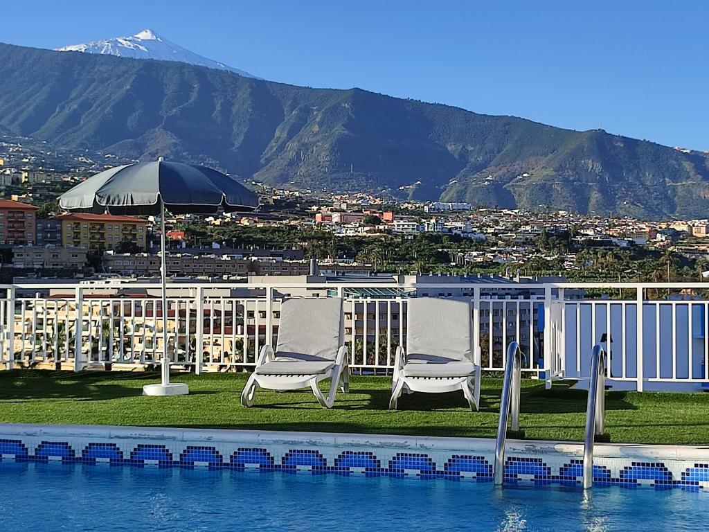 duas cadeiras e um guarda-chuva sentado ao lado da água em Skyview Hotel Tenerife em Puerto de la Cruz