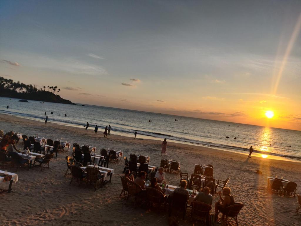 a group of people sitting on the beach at sunset at Rococo Pelton beach huts Palolem Beach goa in Palolem