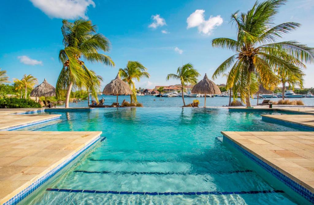 a swimming pool with palm trees and the ocean at La Maya Beach Curacao in Willemstad