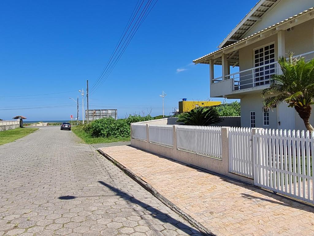 ein Haus mit einem weißen Zaun neben einer Straße in der Unterkunft Ampla casa com 5 quartos e vista para o mar in Navegantes