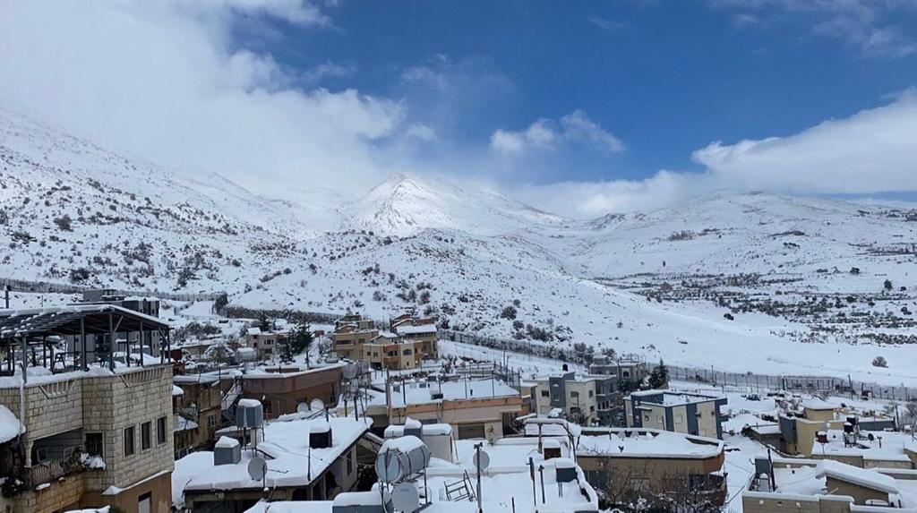 a town covered in snow with mountains in the background at Eastside Suites in Majdal Shams