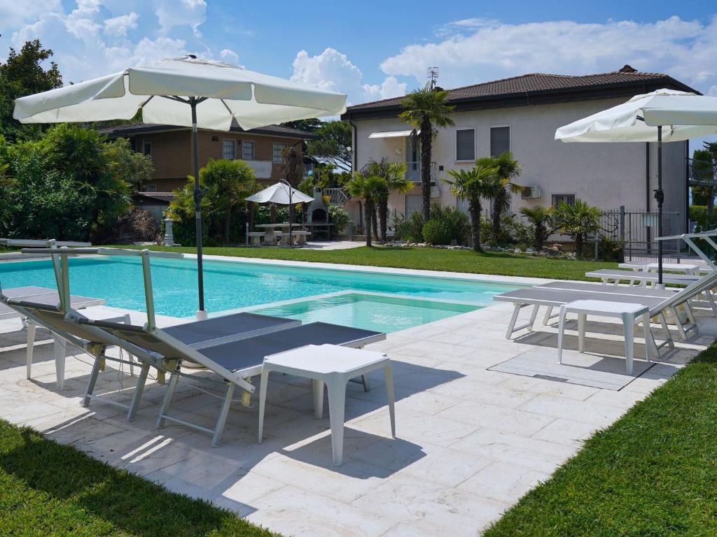 una piscina con 2 sillas y sombrillas, una mesa y bancos en Belvilla by OYO Margherita, en Lazise
