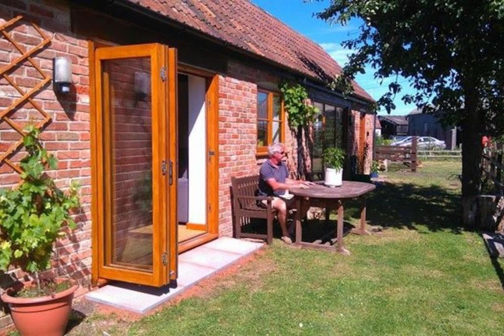 Ein Mann, der an einem Tisch vor einem Backsteinhaus sitzt. in der Unterkunft The Cottage @ Winslade Farm in Bridgwater