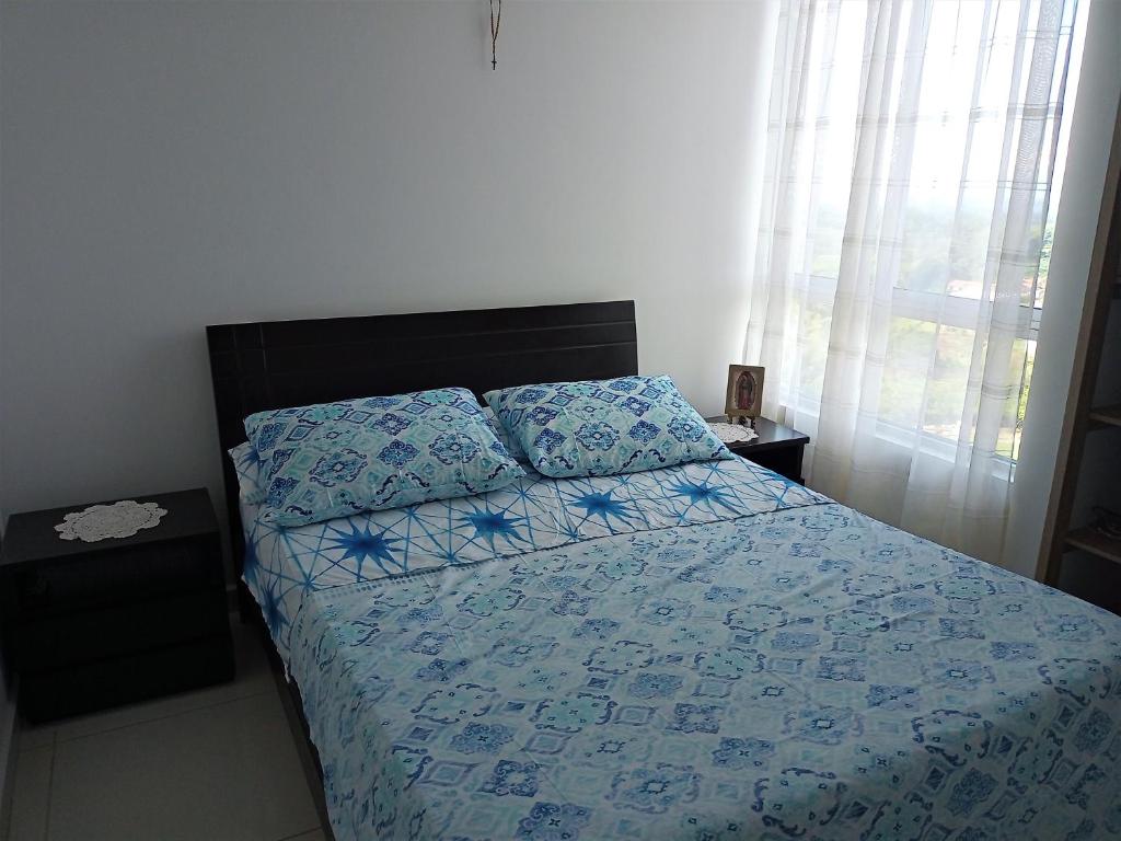 a bedroom with a bed with blue sheets and a window at Apartamento en Armenia cerca al Parque del Café in Armenia