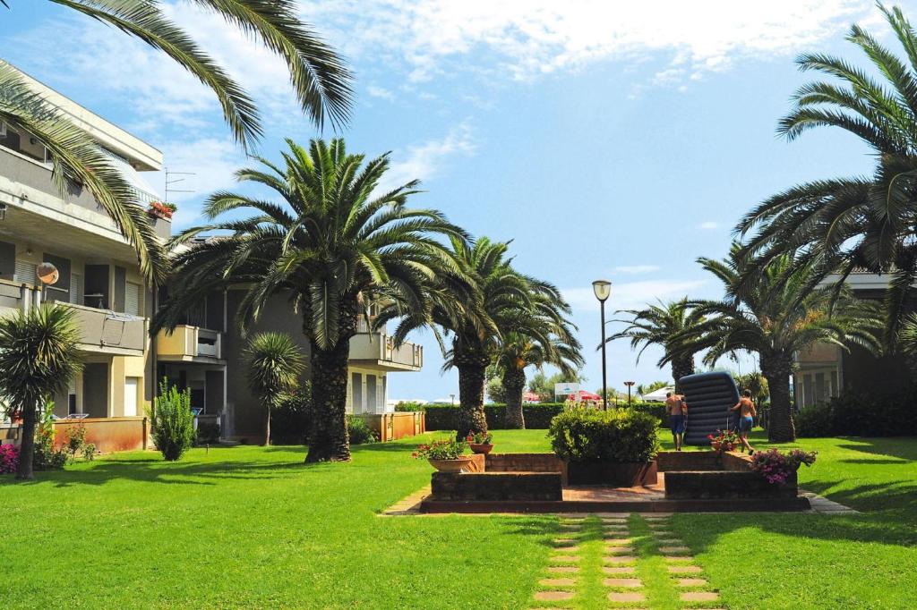 un homme assis sur une chaise dans une cour plantée de palmiers dans l'établissement Apartment in Silvi Marina with parking space, à Silvi Marina