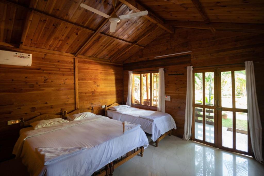 two beds in a room with wooden walls and windows at Oxygen Palolem in Palolem