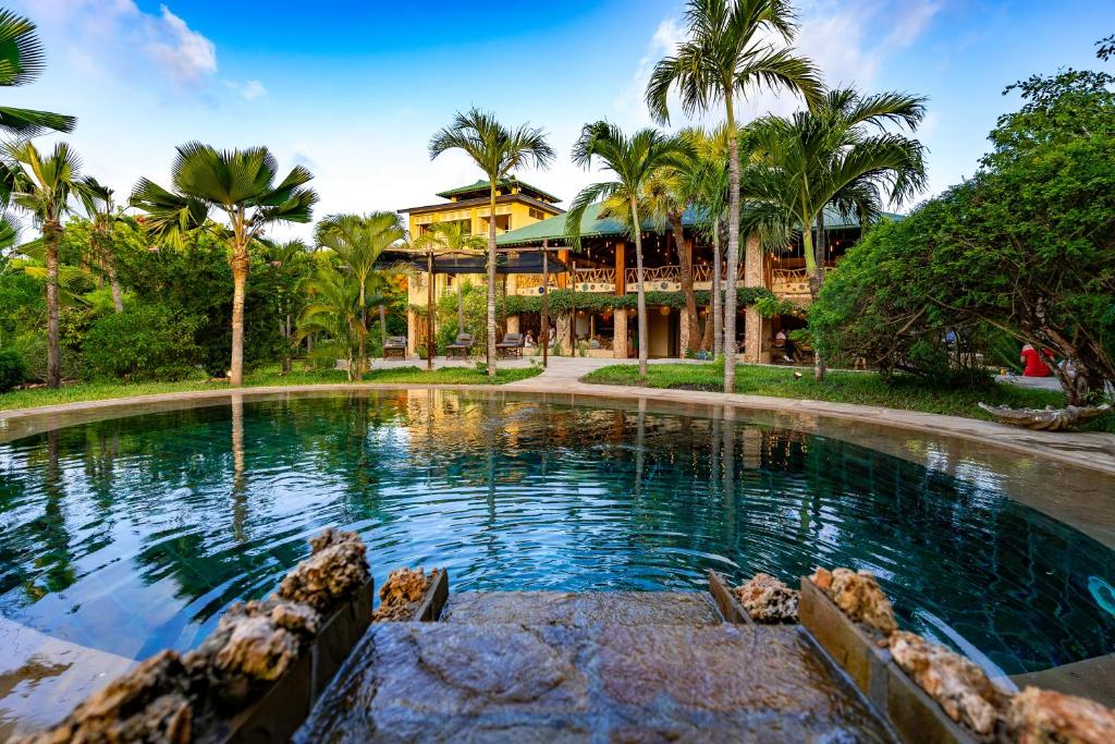 uma piscina em frente a uma casa com palmeiras em Tombo House em Diani Beach