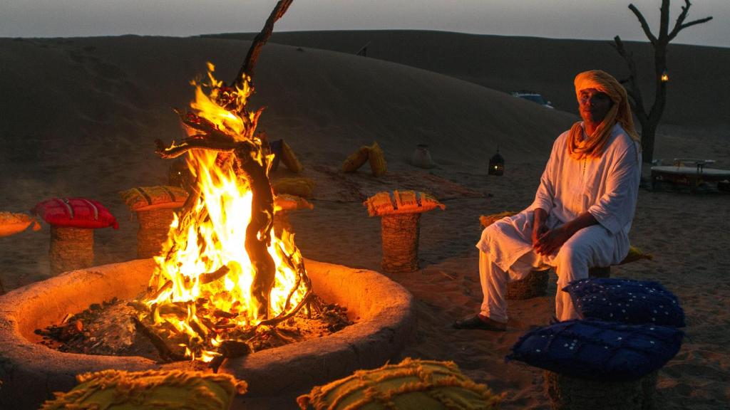 a woman sitting next to a fire pit in the desert at Atta Desert Camp in El Gouera