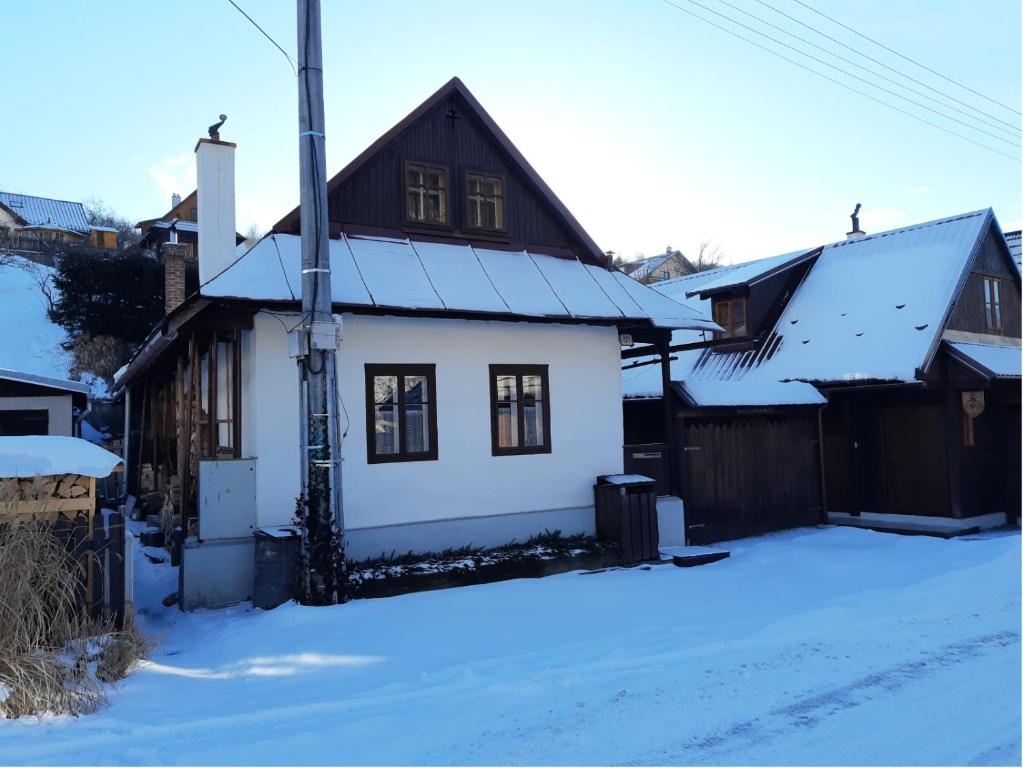 una casa blanca con techo negro en la nieve en U včelárov, en Mýto pod Ďumbierom