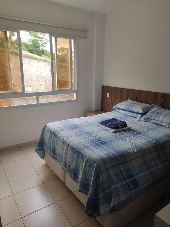 a bedroom with a bed with a blue blanket and two windows at Aconchego Encantador in Viçosa