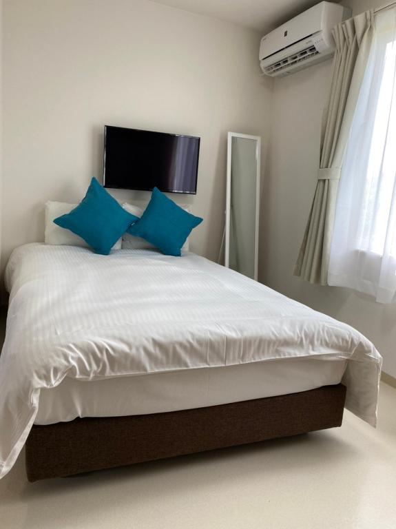 a bedroom with a white bed with blue pillows at PLEASANT STAY Sunayama in Miyako-jima