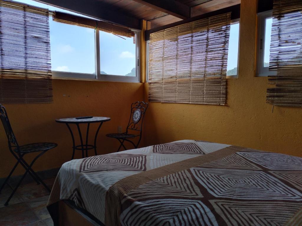 a bedroom with a bed and a table and windows at Hospedaje Casa Verde in Tepoztl&aacute;n