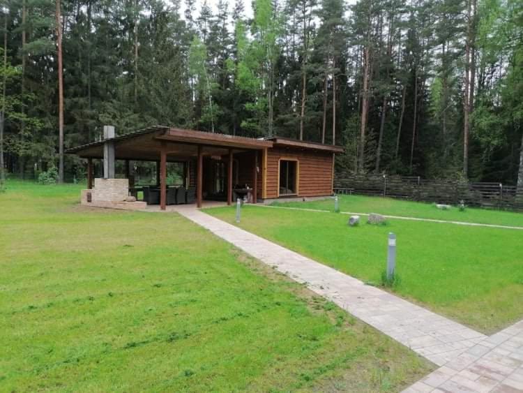 a small cabin in a grassy field with a building at ForrestVila in Karačiūnai