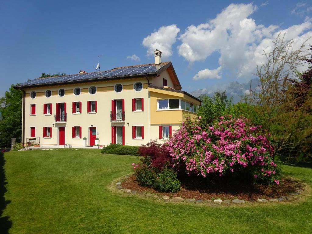 a large white house with red shutters and a bush with pink flowers at Casa Novecento in Feltre
