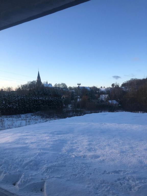 un campo cubierto de nieve con una iglesia en el fondo en Apartamenty Gietrzwałd, en Gietrzwałd